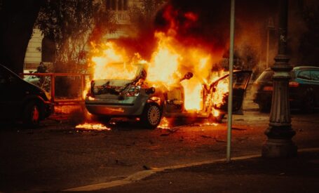 A burning car parked in the street at night resulting in costly property crime